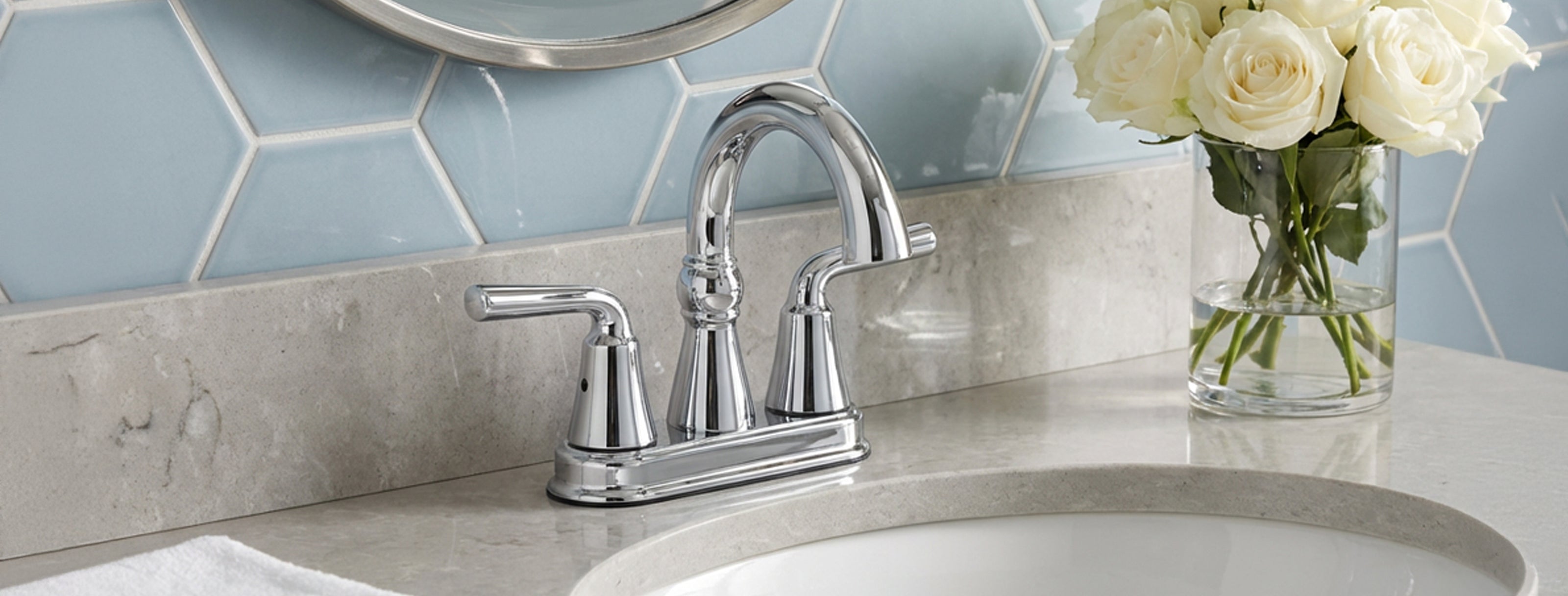 Chrome sink faucet with a vase of white roses on a tiled bathroom wall.