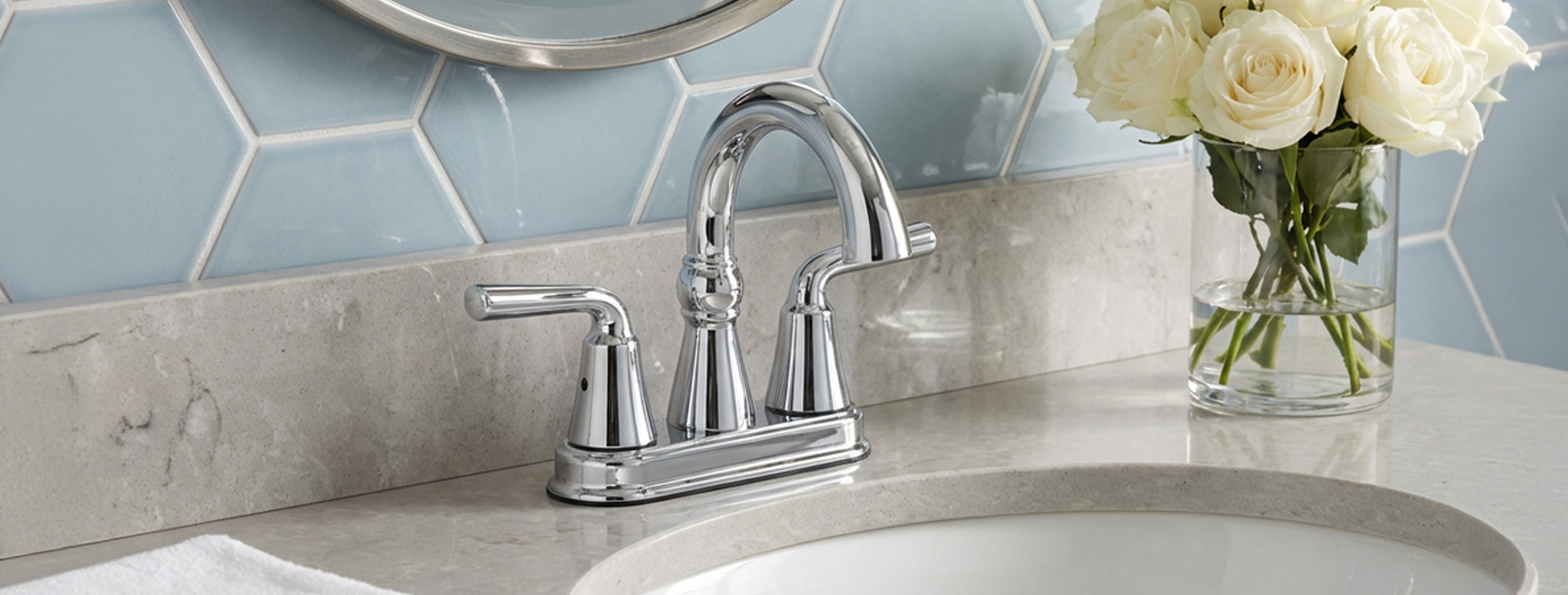 Chrome sink faucet with a vase of white roses on a tiled bathroom wall.