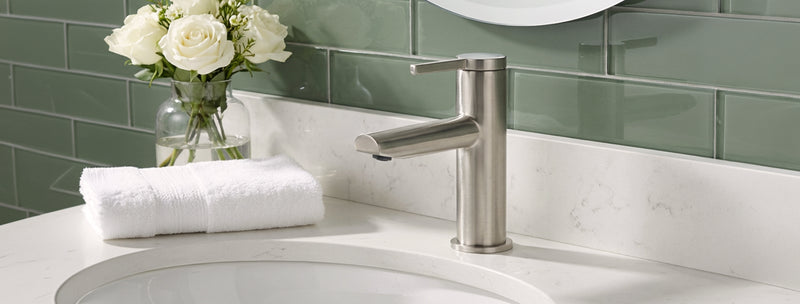 Bathroom sink with faucet, white towels, and flowers on a green tiled wall.