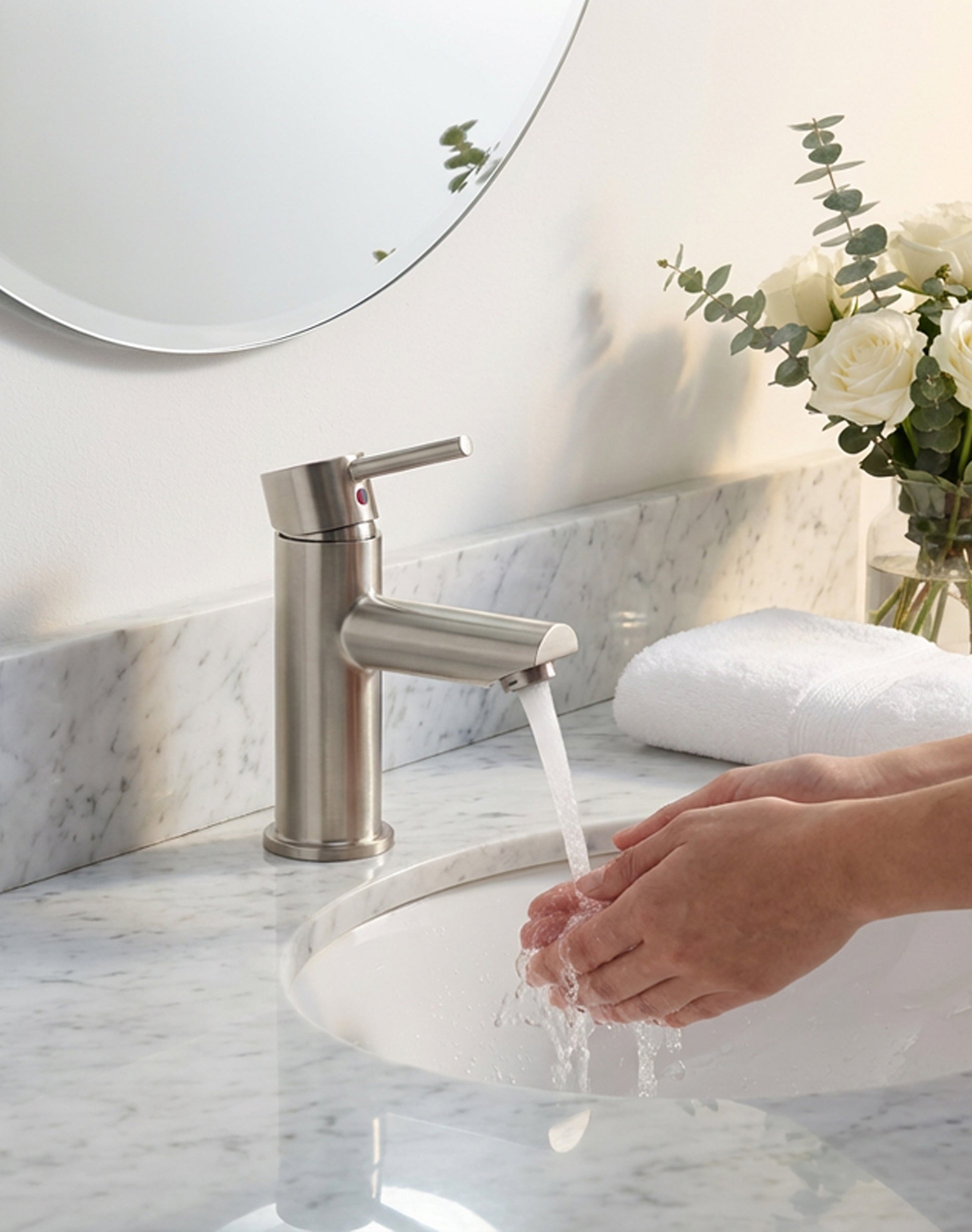 Person washing hands under a modern faucet in a bathroom with marble countertop and decorative elements.