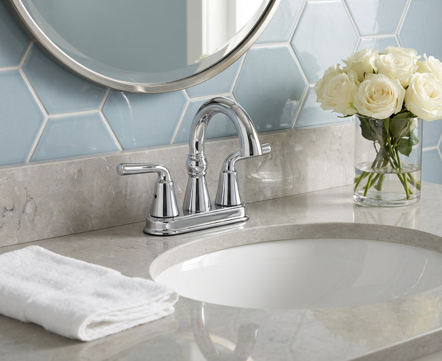 Bathroom sink with silver faucet, white roses in a vase, and hexagonal tile backsplash.