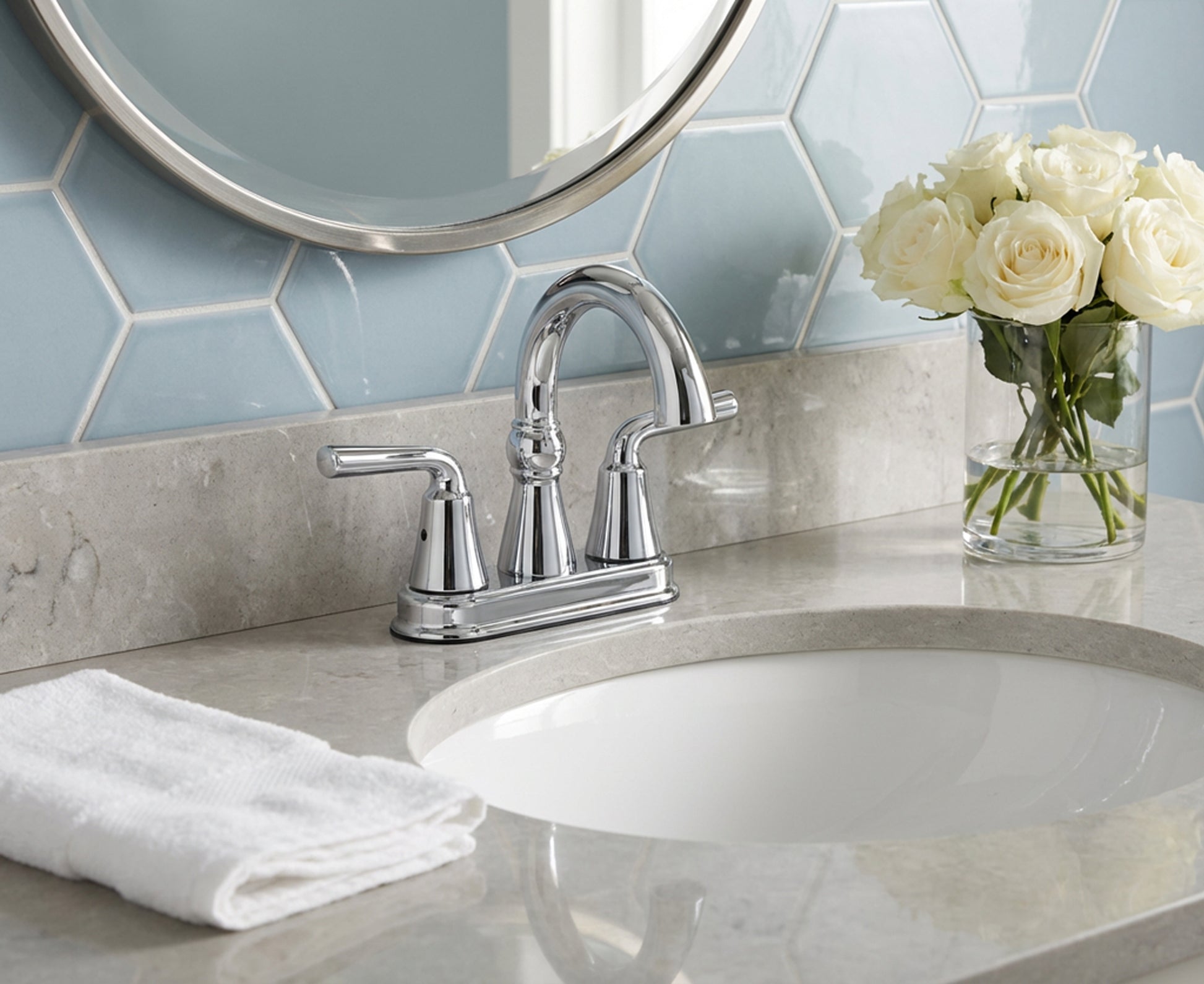 Bathroom sink with silver faucet, white roses in a vase, and hexagonal tile backsplash.