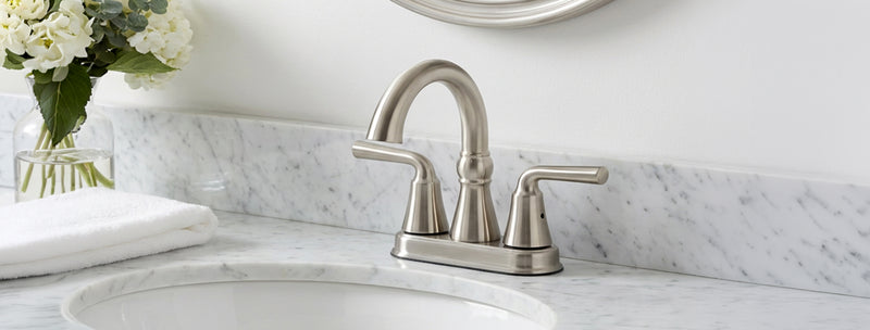 Silver faucet on a white sink with marble countertop and decorative flowers.
