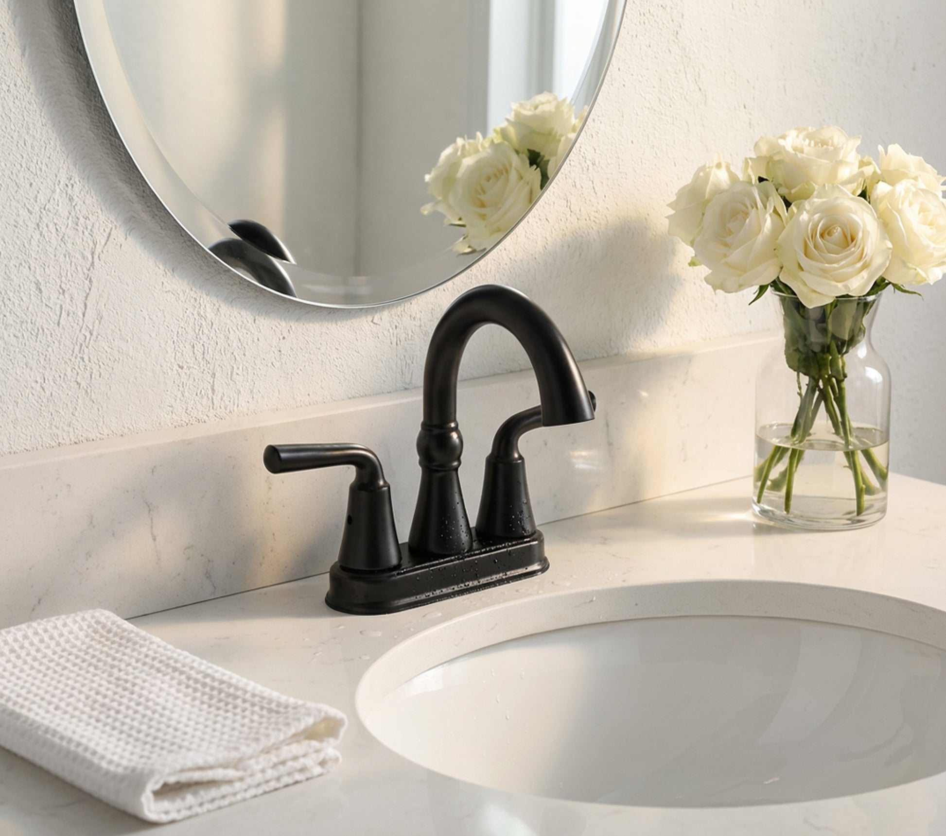Bathroom sink with black faucet, white roses in a vase, and a towel on a marble countertop.